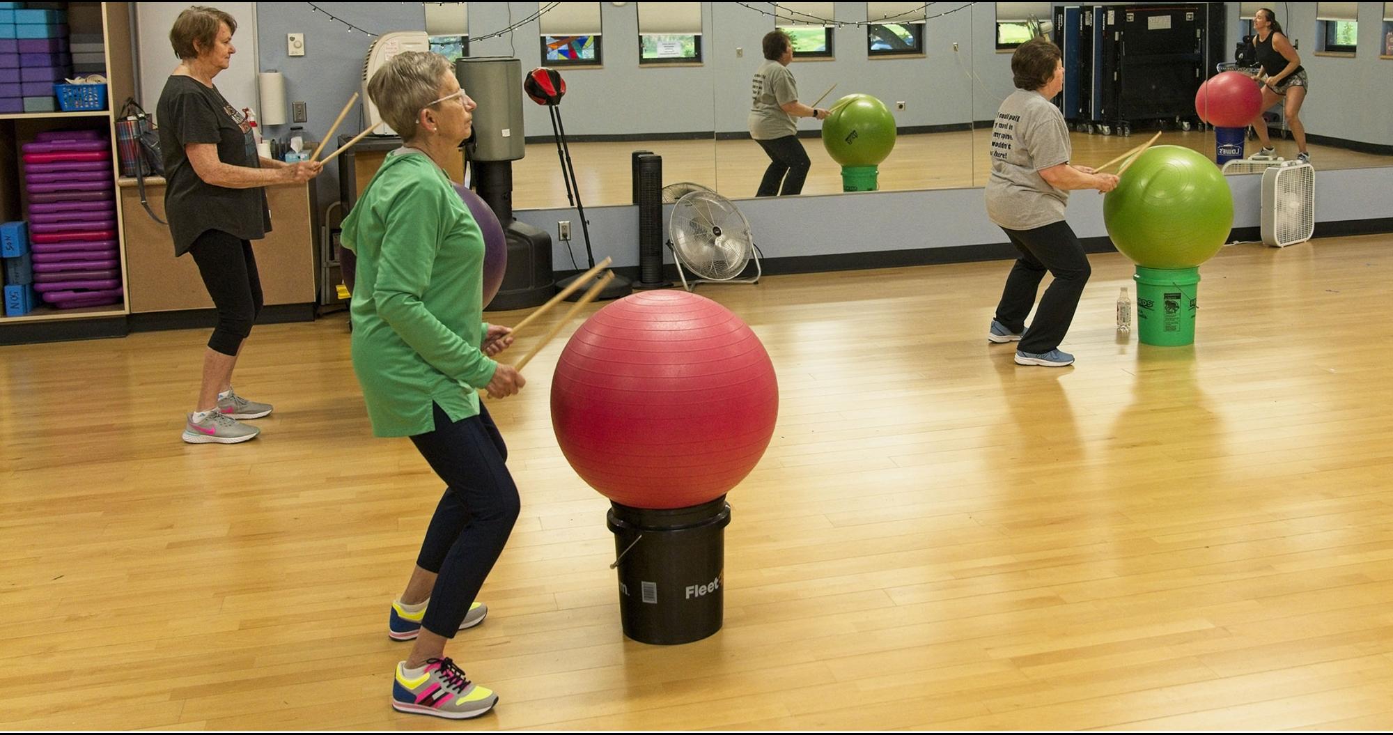 Women hitting large balls with drumsticks